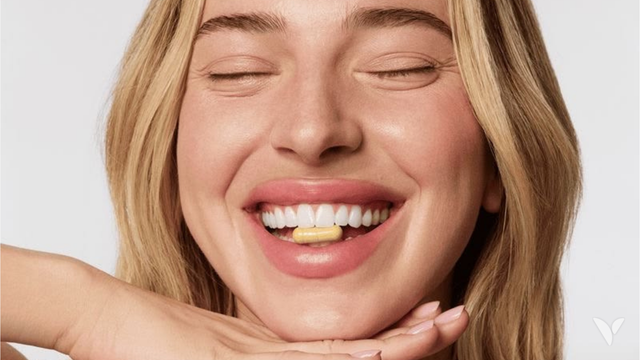 Femme souriante tenant une gélule de complément vitamine B12 entre les dents
